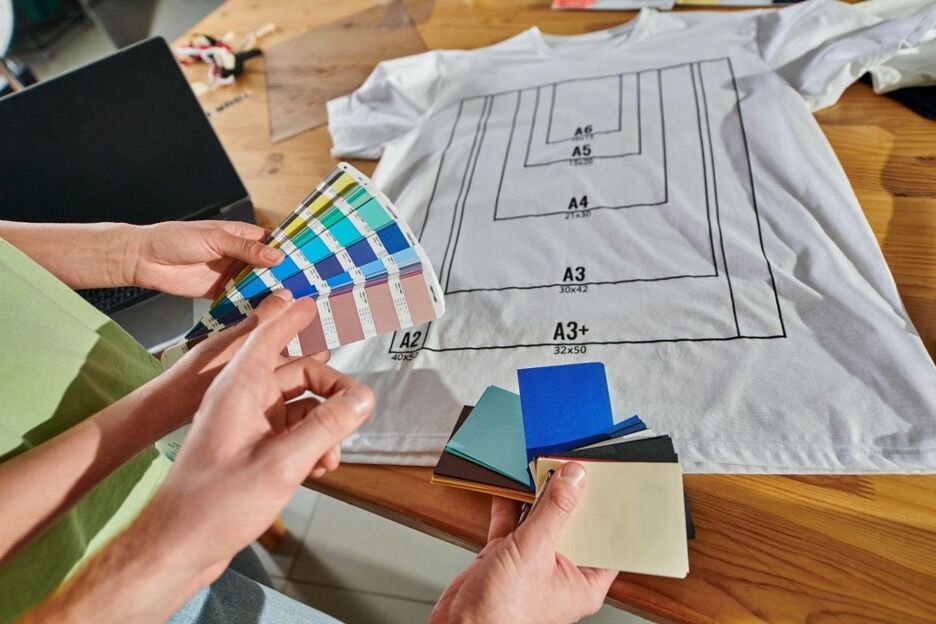 A cropped view of a craftsman pointing at color swatches held by a colleague while discussing custom shirt design options.
